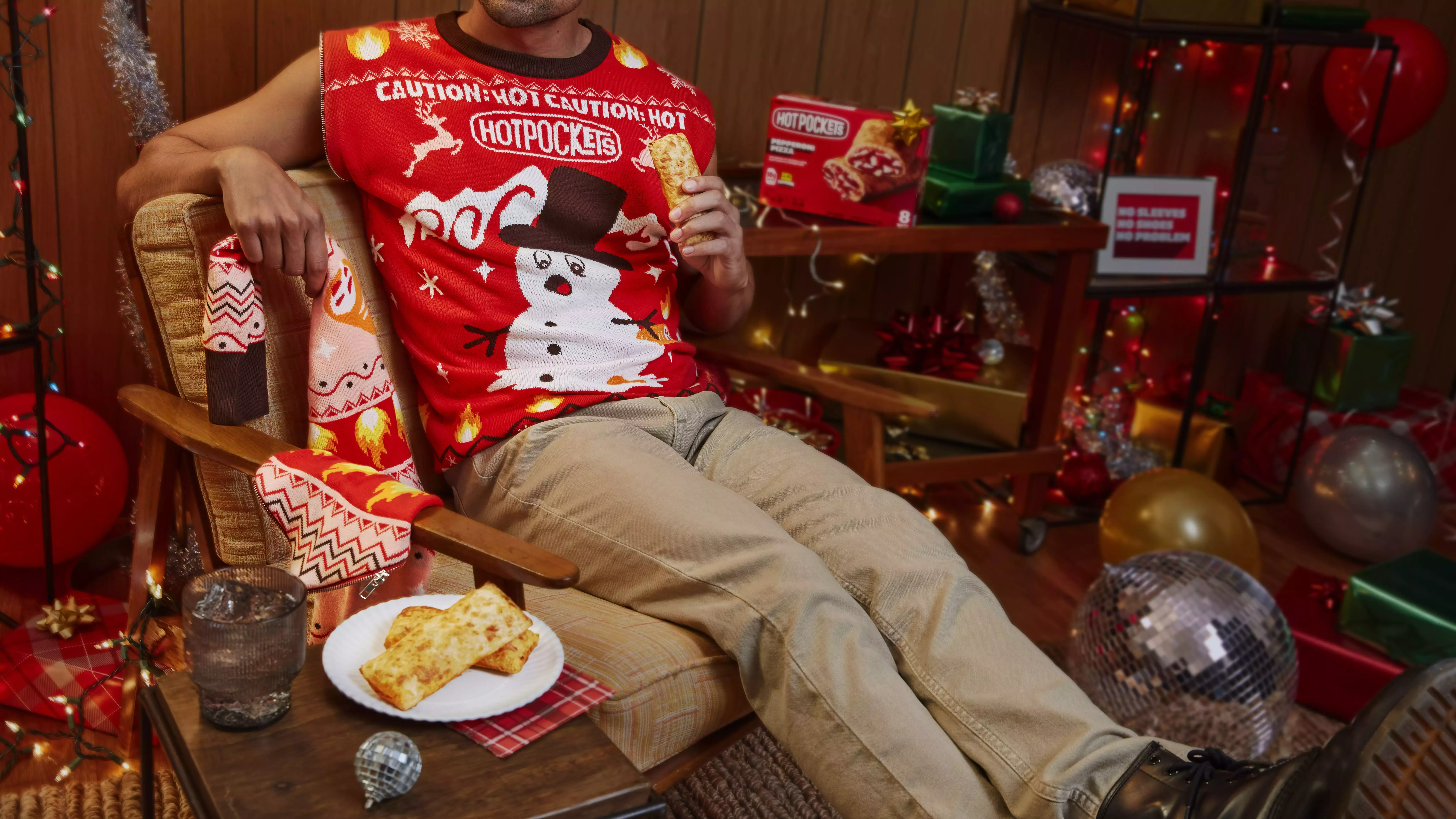 Man sitting in chair eating Hot Pocket in sleeveless holiday sweater